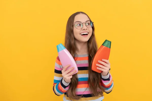 kid in glasses holding shower gel. happy teen girl use shampoo bottle. child with hair conditioner