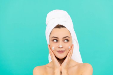 Neşeli genç bayan mavi arka plana yüz kremi sür.