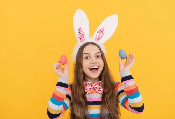 Niño feliz en orejas de conejo y corbata de lazo sostienen huevos de Pascua sobre fondo amarillo —  Fotos de Stock