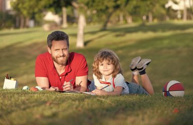 Baba ve oğul parkta çimenlerde rahatlar çizim yapmayı öğrenir, aile hafta sonu