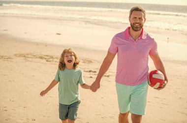 Spor aktivitesi. Gülümseyen baba ve oğul kumsalda topla yürür. Baba ve çocuk çocuk.