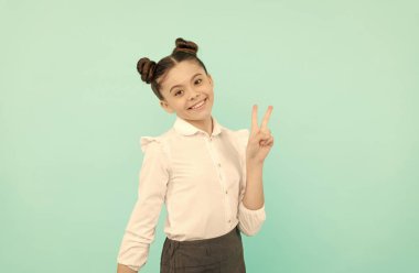 Mutlu kız çocuğu okula geri döndü V işaretini gösteriyor el hareketi mavi arka plan, zafer