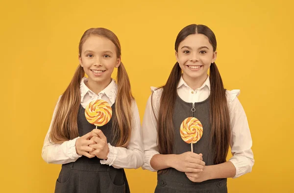 Niños felices en uniformes escolares sostienen piruletas fondo amarillo, dientes dulces —  Fotos de Stock