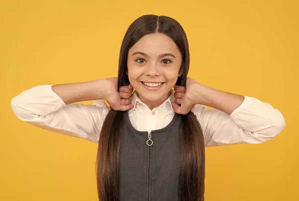 Niña feliz en uniforme escolar sonrisa sosteniendo el pelo largo fondo amarillo, salón — Foto de Stock