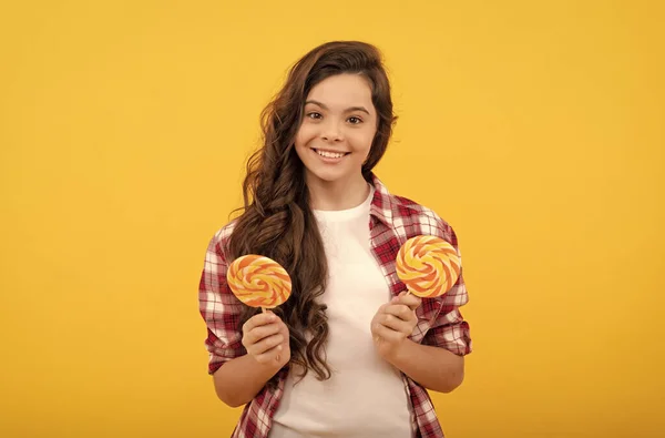 Gelukkig tiener meisje met krullend haar hold lolly karamel snoep op gele achtergrond, karamel winkel. — Stockfoto