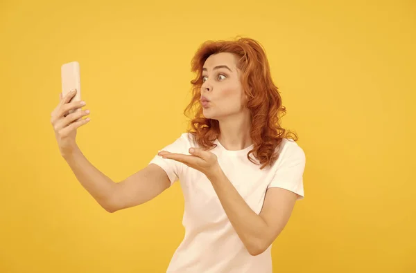 Chica hacer gesto de besar la mano a la cámara teléfono fondo amarillo, dispositivo móvil —  Fotos de Stock