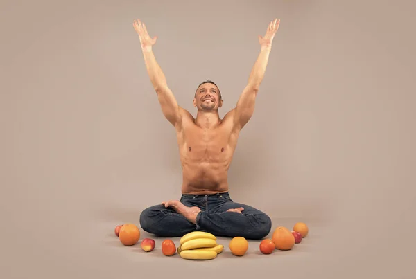 El hombre atlético se sienta en posición de loto con las manos levantadas y fruta orgánica natural, nutrición de yoga. —  Fotos de Stock