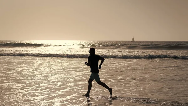 Wysportowany człowiek biegacz sylwetka biegać na letniej plaży z wodą morską i słońcem, wytrzymałość — Zdjęcie stockowe