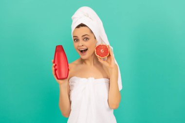 Mavi arka planda greyfurt şampuanı şişesi olan havluyla hayrete düşmüş bir kız.