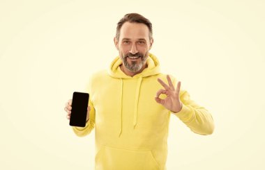 Kapüşonlu mutlu ve olgun bir adam akıllı telefon ekranı sunuyor. Kopyalama alanı beyaza izole edildi, tamam mı?.