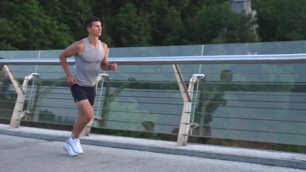Athletischer muskulöser Mann in Sportbekleidung läuft morgens auf gläserner Brücke, laufe — Stockvideo