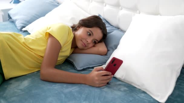 Niño sonriente charlando en el teléfono inteligente en la cama, relajarse — Vídeo de stock