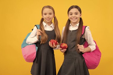 Resmi üniformalı aç çocuklar okulda atıştırmak için vitamin elması tutarlar sarı arka plan, atıştırma