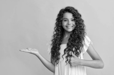 Uzun kıvırcık saçlı ve cilt sunan mutlu çocuk başparmağını kaldır, kopyala, reklam yap..