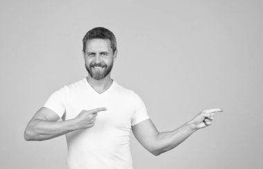 Beyaz tişörtlü mutlu yakışıklı adam gülümsüyor. Parmakla işaret ediyor. Reklam jesti, reklam.