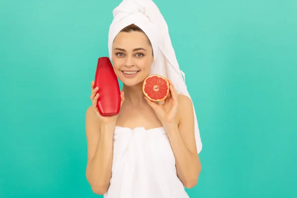 Happy lady in towel with grapefruit shampoo bottle on blue background — Stock Photo, Image