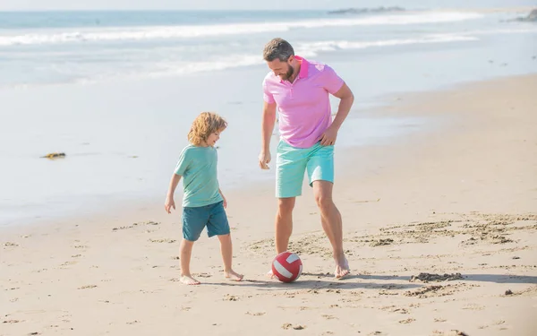 Pai e filho sorridentes jogam futebol na praia. papai com menino no dia de verão. — Fotografia de Stock