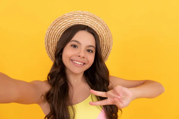 Счастливый ребенок в летней соломенной шляпе делает селфи на желтом фоне, мир — стоковое фото