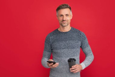 Mutlu adam fincandan kahve içiyor ve kırmızı arka planda telefon kullanıyor. İletişim.