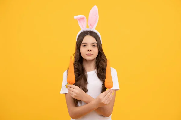 Niño serio en orejas de conejo sostienen zanahoria sobre fondo amarillo, Pascua —  Fotos de Stock