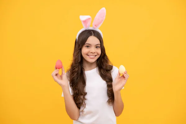 Uśmiechnięta nastolatka dziewczyna w króliczych uszach trzymać jaja na żółtym tle, Wielkanoc — Zdjęcie stockowe