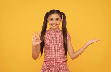 Mutlu çocuk ürünü sarı arka planda sunuyor. Kopya alanı gösterisi. Tamam, reklam ver.