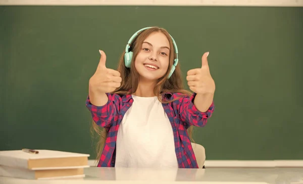 Happy kid with earphones at blackboard showing thumb up, ebook — Stock Fotó