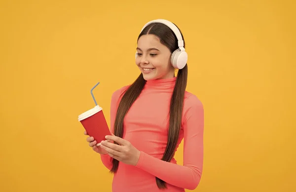 Heureux adolescent fille écouter de la musique dans les écouteurs avec tasse en papier sur fond jaune, matin — Photo