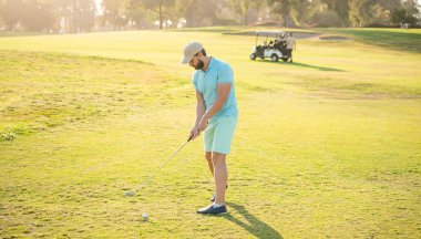 Profesyonel sahada, yeşil çimenli, golf salıncaklı konsantre erkek golfçü.