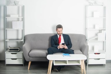 İş adamı ofisinde oturuyor ve telefonda mesajlaşıyor.