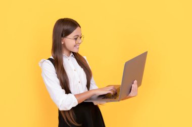 Okul üniformalı ve gözlüklü mutlu genç kız laptopta çalışıyor, eğitim görüyor.