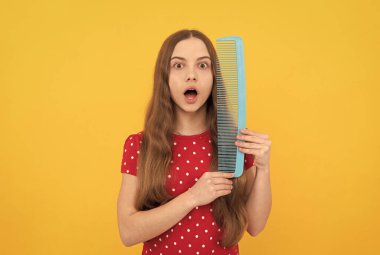 Şaşkın çocuk uzun saç fırçası sarı arka planda, kuaför