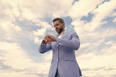 Takım elbiseli yakışıklı, olgun iş adamı. Kol saatini kontrol et. Gökyüzü arka planında, dakiklik..