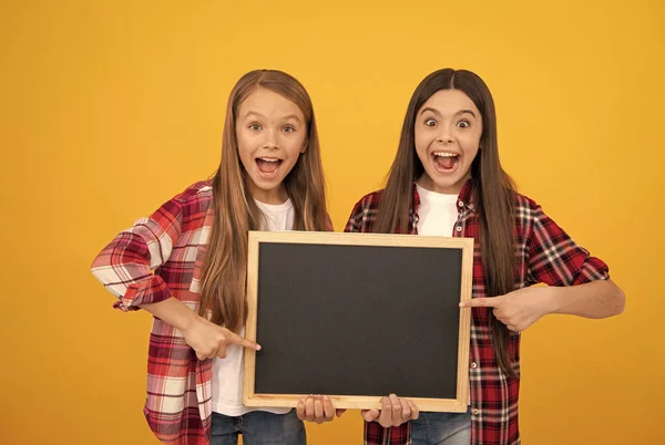 Sorprendido adolescente niñas en casual a cuadros dirigiendo a la escuela pizarra para el espacio de copia, ofreciendo —  Fotos de Stock