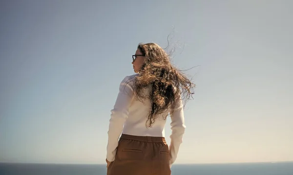 Jej włosy płyną na wietrze. Kobieta z długimi włosami stoi na morzu. Stylowa dziewczyna z falistą fryzurą — Zdjęcie stockowe