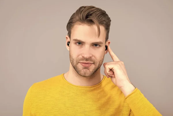 Handsome guy point finger at earbud headphones inside ear grey background, listening — Stock Photo, Image