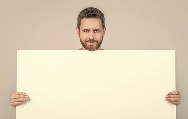 Smiling mature bearded man behind blank white paper banner with copy space for offer, presentation — стоковое фото