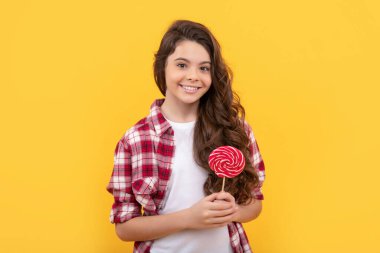 Uzun kıvırcık saçlı neşeli çocuk sarı arka planda lolipop karamel şeker tutuyor, diş bakımı....