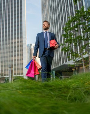 Takım elbiseli kendine güvenen girişimci elinde alışveriş çantası ve hediye kutusu tutuyor, sevgililer günü..