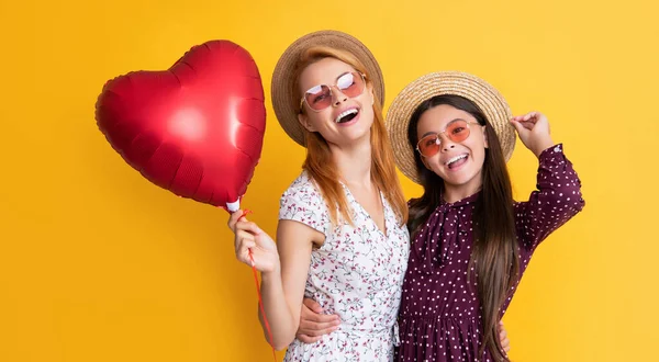 Mother and daughter smile hold love heart balloon on yellow background — стоковое фото