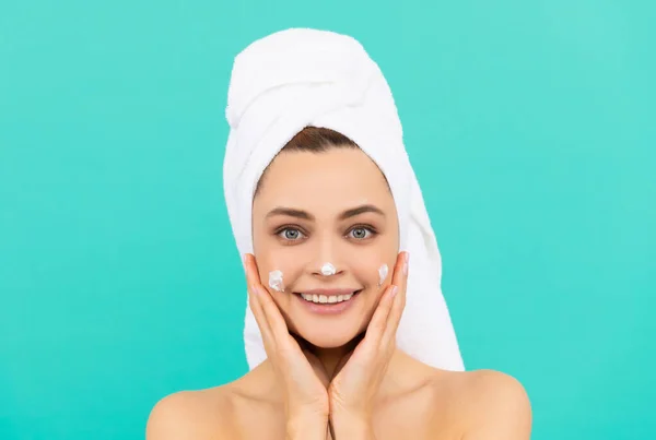 Šťastná mladá žena použít krém na obličej na modrém pozadí — Stock fotografie