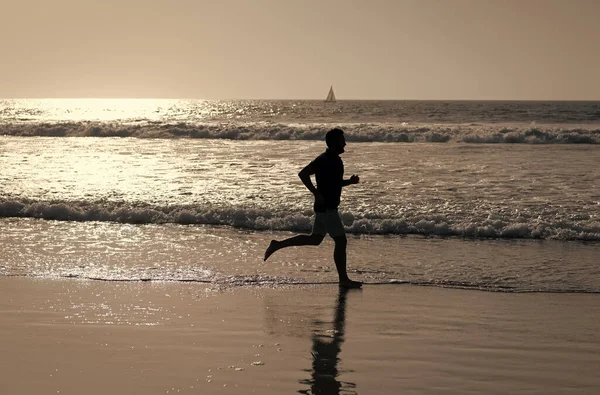 Wysportowany człowiek biegacz sylwetka biegać na letniej plaży z wodą morską i słońcem, sport — Zdjęcie stockowe