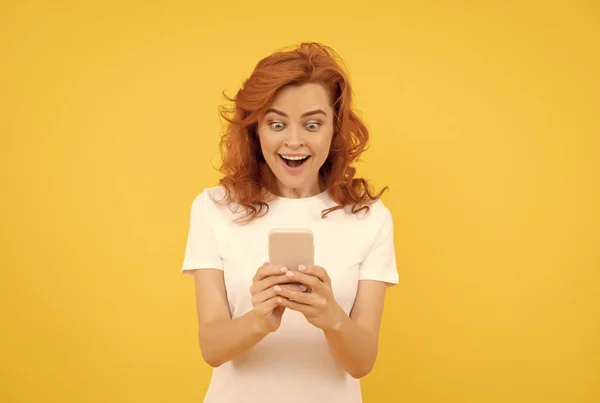 Förvånad kvinna chatta i smartphone eller göra online shopping på gul bakgrund, känslor. — Stockfoto