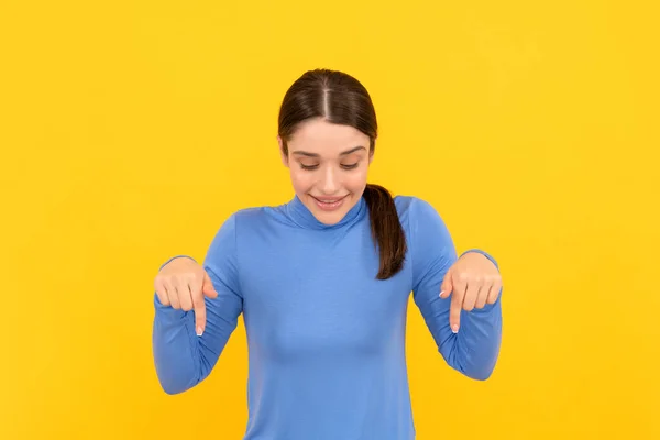 Woman portrait pointing fingers down on copy space yellow background, presenting — kuvapankkivalokuva