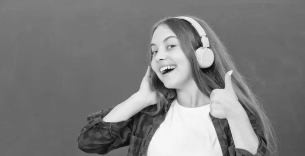 Happy girl hold modern headphones in high school at blackboard showing thumb up, audio accessory. — Stock Photo, Image