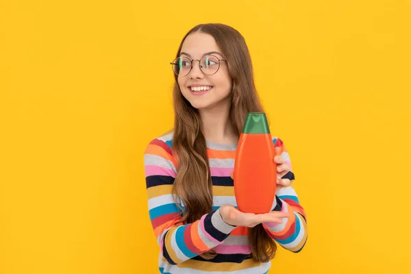 Cheerful child long hair in glasses showing shower gel bottle, advertising — Stock fotografie