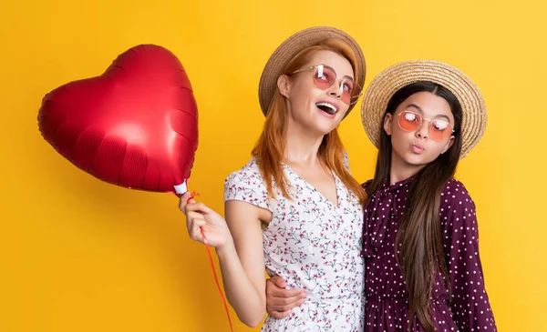 Neşeli anne ve kızı sarı arka planda aşk balonu tutuyorlar.