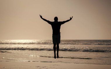 Yaz plajında zıplayan atletik bir adamın silüeti, özgürlük.