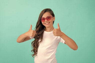 Mutlu çocuk güneş gözlüğü takan kıvırcık saçlı mavi arka planda, yaz tarzında.