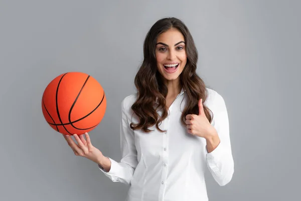 Ευτυχισμένη γυναίκα με τον αντίχειρα ψηλά κρατώντας μια μπάλα του μπάσκετ, απομονωμένη σε γκρι φόντο. — Φωτογραφία Αρχείου